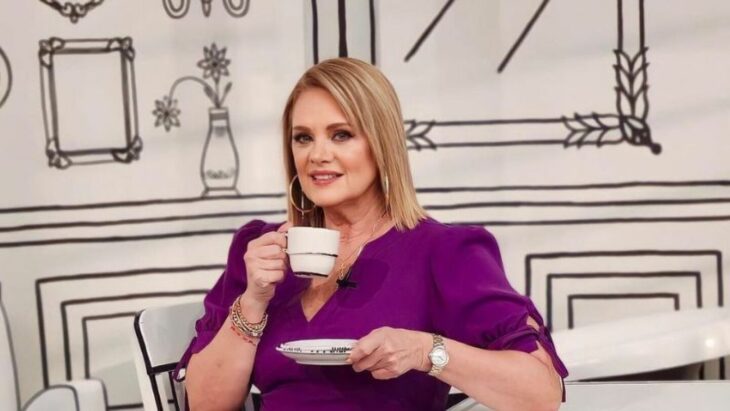 Erika Buenfil sentada tomando una taza de café con paredes dibujadas que simulan una cocina