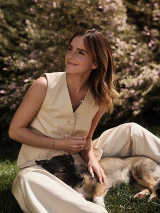 Emma Watson sentada en un césped con un perro entre sus piernas 