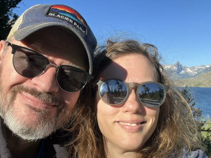 una pareja sonríe a la cámara en una imagen de su rostro ambos llevan lentes de sol y él luce una gorra gris
