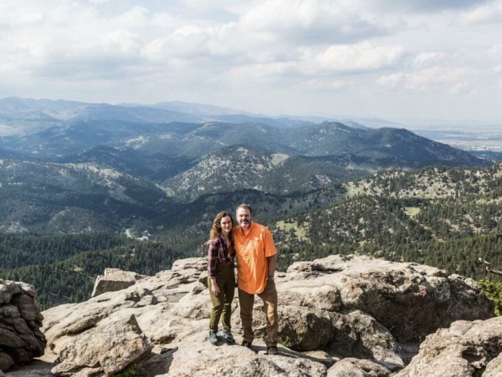 una pareja se abraza y posa de frente en una montaña el paisaje de las alturas es impresionante