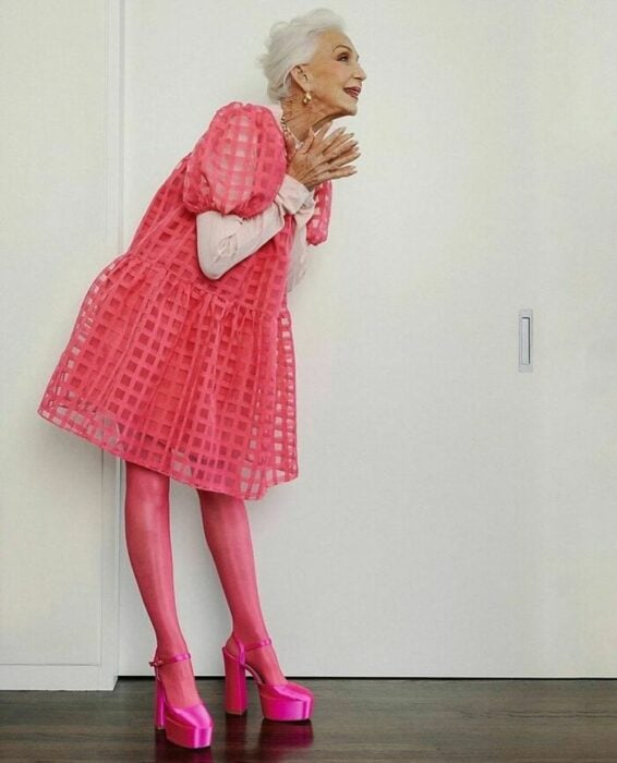 una modelo de 74 años posa con un vestido rosa juvenil lleva zapatos altos y medias de color