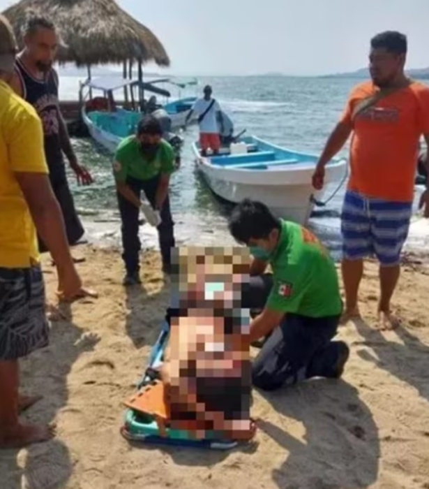 personal de la Cruz Roja atiende a una persona que está tirada en la playa sobre una camilla varias personas observan alrededor
