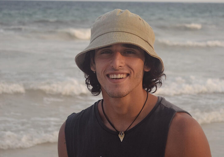 un chico está sonriente en la playa lleva un gorro de pescador color crema