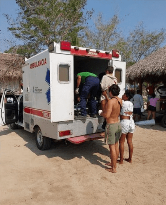 una ambulancia esta abierta mientras personal acomoda a una persona que será trasladada otros observan la escena