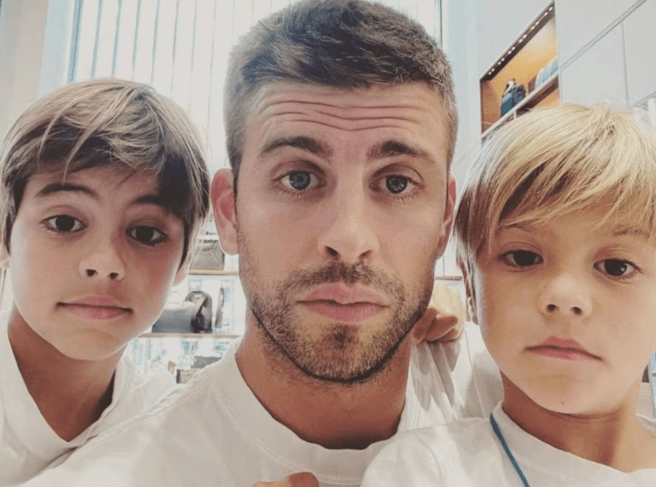 Gerard Piqué posando para la cámara junto a Milán y Sasha los hijos que tuvo con Shakira están en una habitación frente a a cámara y todos visten playera blanca