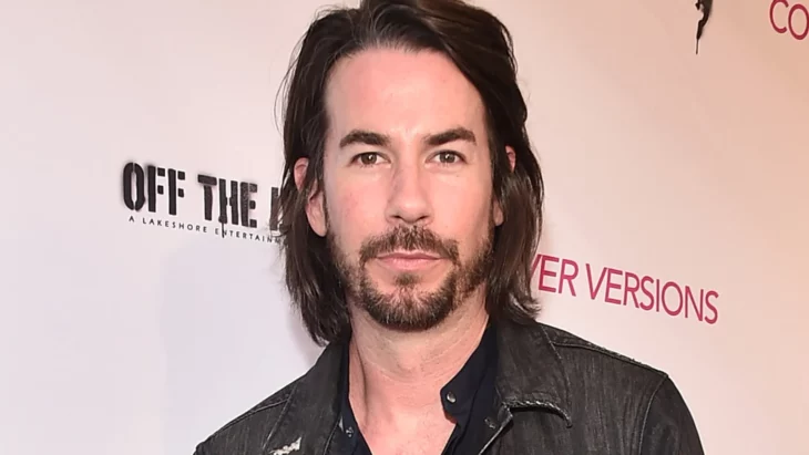 Jerry Trainor con el cabello hasta los hombros y barba con bigote está posando en algún evento