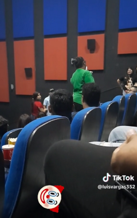 personas sentadas en una sala de cine con asientos azules mientras una mujer de pie les da indicaciones