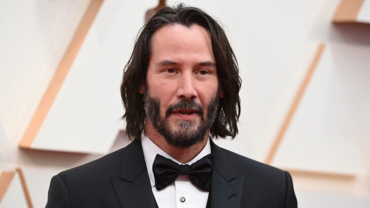 Keanu Reeves posa en una alfombra roja con esmoquin negro lleva el cabello largo