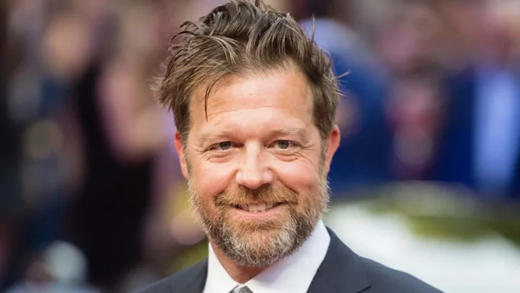 el actor y director David Leitch posa afuera de un evento lleva traje y corbata tiene una barba marcada y el cabello desaliñado