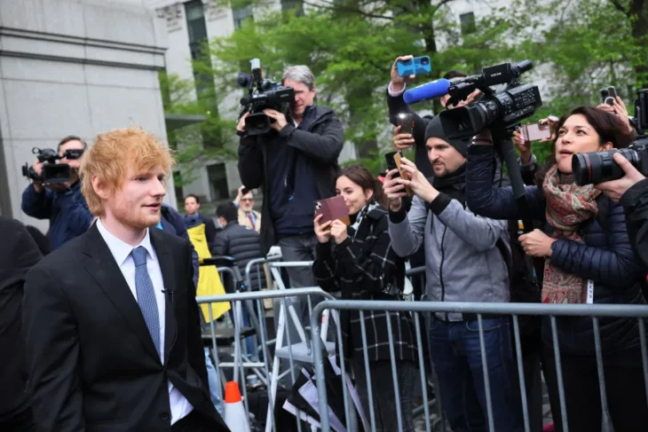 Ed Sheeran rodeado de reporteros a la salida de la Corte de Nueva York lleva un traje oscuro con corbata