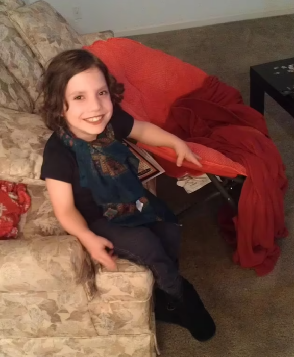 una niña con enanismo sonríe sentada en la sala de una casa 