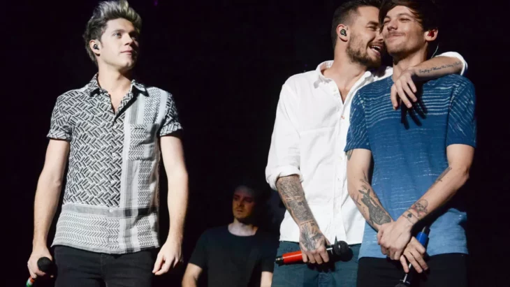 tres de los integrantes del extinto grupo One Direction estan en el escenario llevan micrófonos dos de ellos están abrazados 