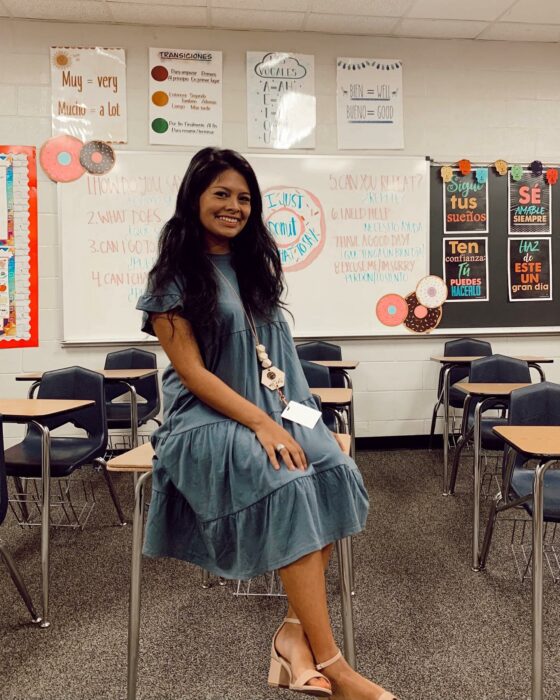 Fotografía de una maestra sentada en una butaca dentro de un salón de clases 