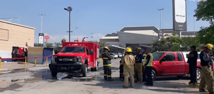 un camión rojo de bomberos estacionado en una plaza comercial bomberos con cascos amarillos y uniforme están platicando luego de atender una emergencia