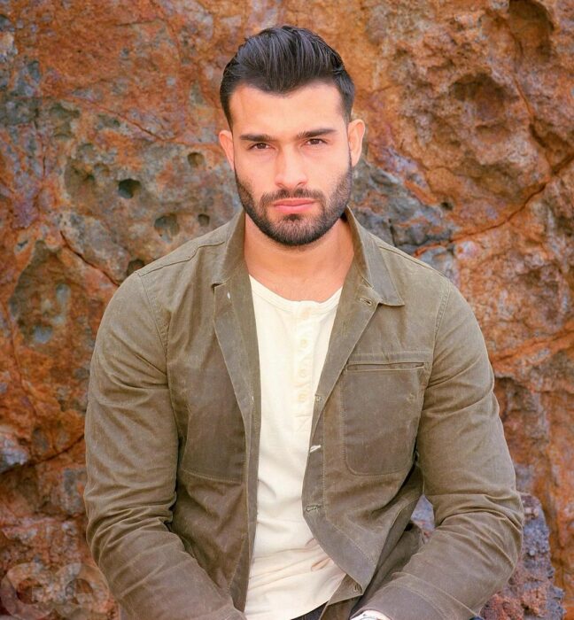 Sam Asghari sentado con chaqueta marrón 