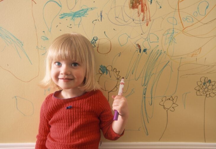 niña dibujando en las paredes con una crayola