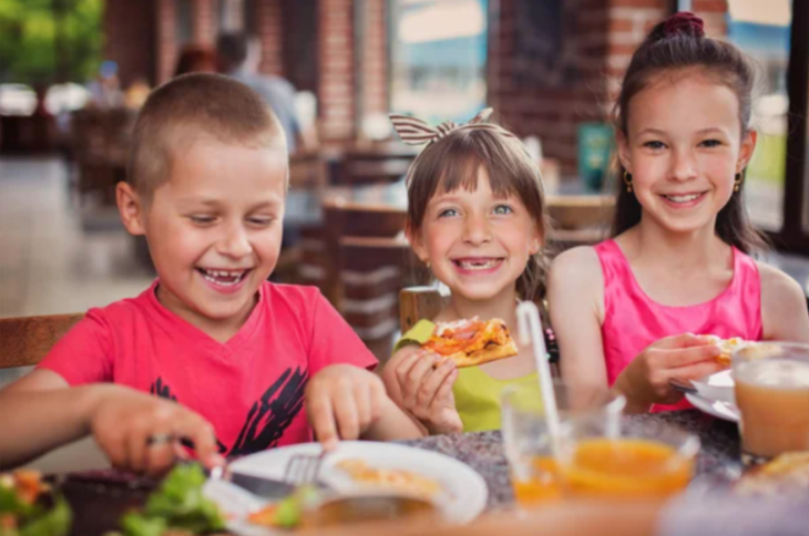 imagenes de dos niñas y un niño comiendo sentados a la mesa de un restaurante los tres sonríen