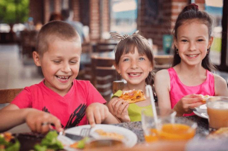 imagenes de dos niñas y un niño comiendo sentados a la mesa de un restaurante los tres sonríen