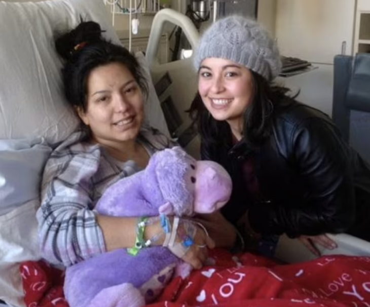 una chica está recostada en una cama de hospital con un peluche morado en sus brazos la acompaña su amiga