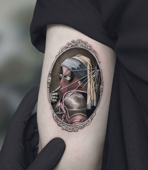 tatuaje de la cara del cuadro de la chica con pendiente de perlas con la cara de Deadpool