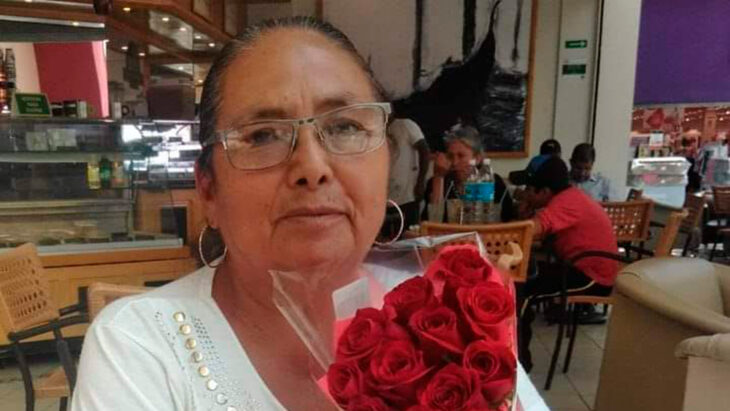 una mujer con lentes está sentada en una mesa de restaurante lleva en sus manos un ramo de rosas rojas 