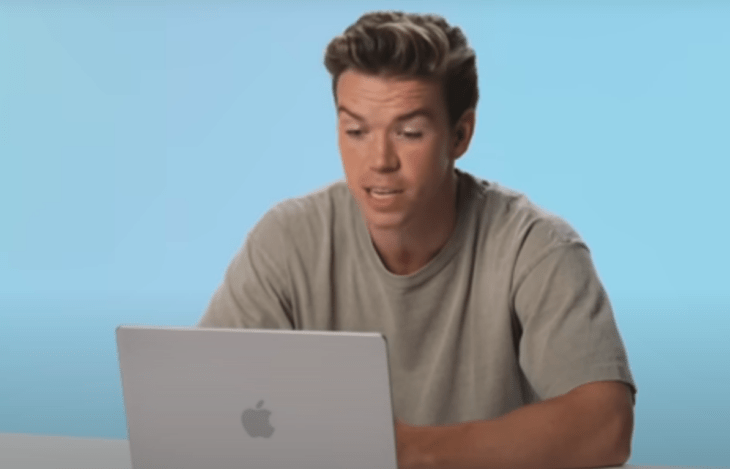 Will Poulter está sentado frente a una computadora su expresión es de asombro