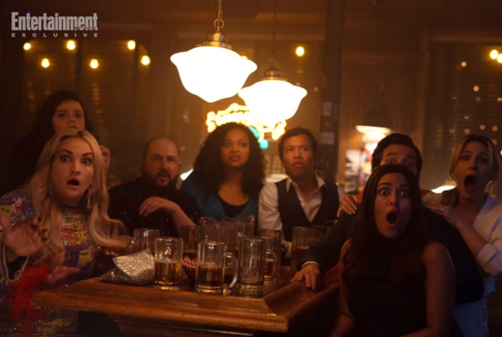 una imagen del reparto de Zoey 102 están sentados alrededor de una mesa con luz tenue y bebiendo cervezas 