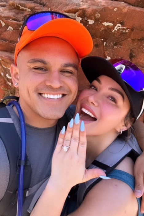Chiquis Rivera y Emilio Sánchez posan sonrientes ambos con gorra ella presume su anillo de compromiso mostrando su mano