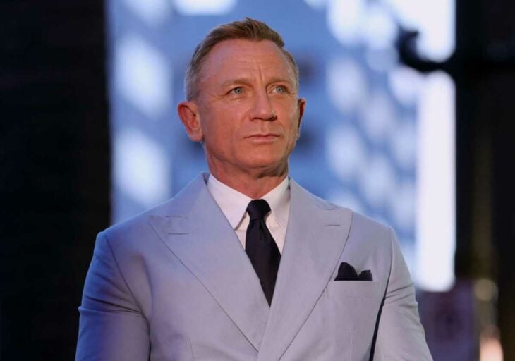 Daniel Craig mira a lo lejos con un semblante serio lleva un traje gris claro