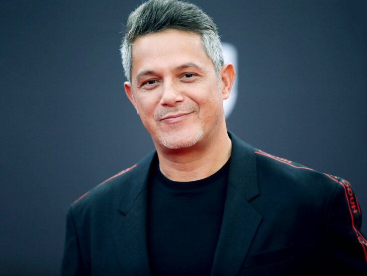 Alejandro Sanz posa con una ligera sonrisa tiene el cabello canoso y lleva ropa oscura