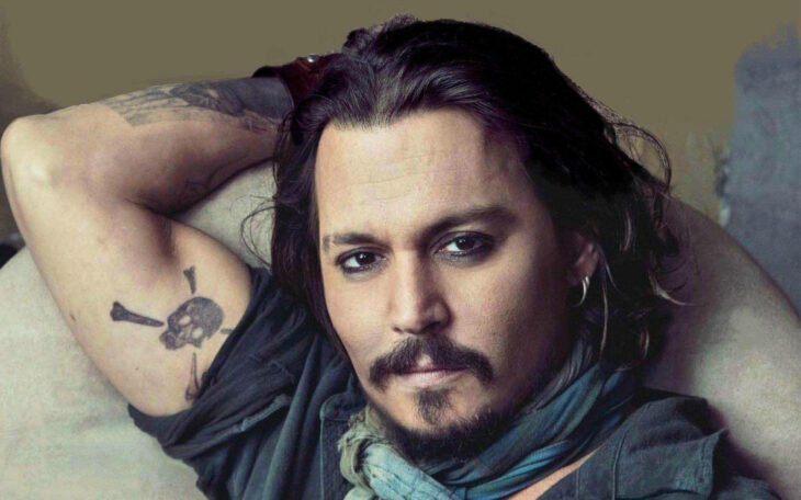 Johnny Deep posando para la cámara con un brazo hacia atrás sosteniéndose la cabeza lleva delineador negro en los ojos y barba con bigote