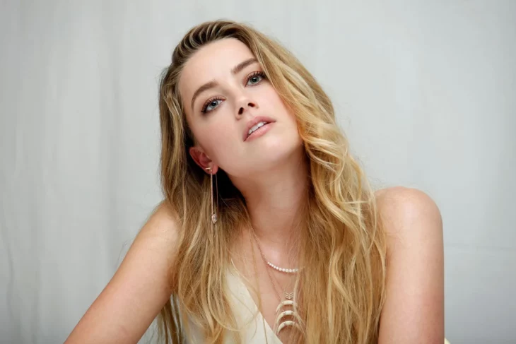 Amber Heard con la cabeza ladeada mirando hacia arriba lleva el cabello suelto y maquillaje