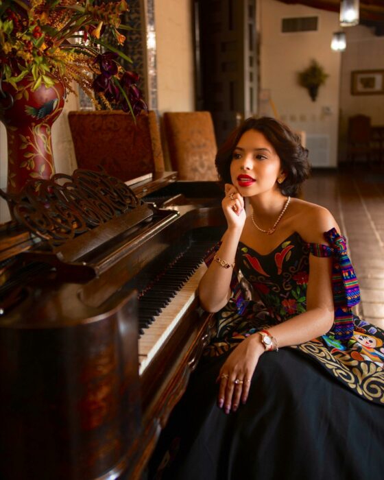 Fotografía de Ángela Aguilar sentada frente a un piano