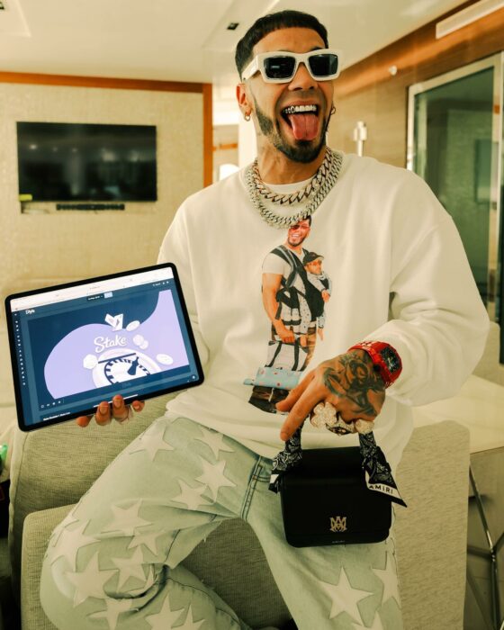 Anuel AA usando una sudadera con estampado cargando a un bebé con la cara de Feid 