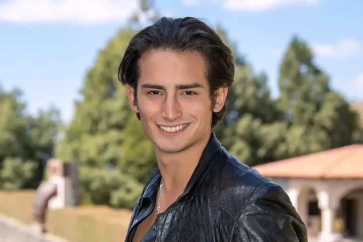 Emilio Osorio posa sonriente en un jardín exterior está vestido de negro