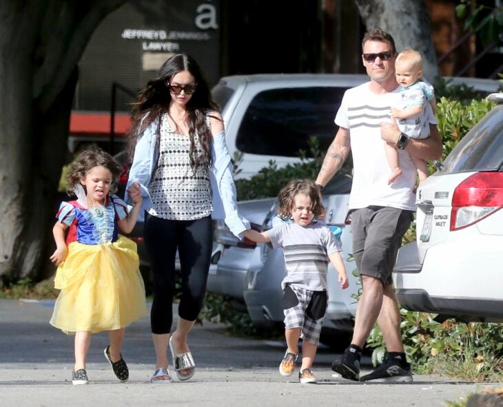 Megan Fox posando con sus hijos vestidos de mujer caminando entre unos autos 