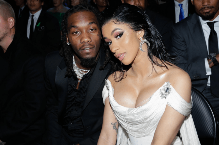 Cardi B y Offset posan en un evento están sentados entre el público ella lleva un vestido de noche de color blanco con arracadas de diamantes él esta vestido de negro y lleva gruesas cadenas en el cuello