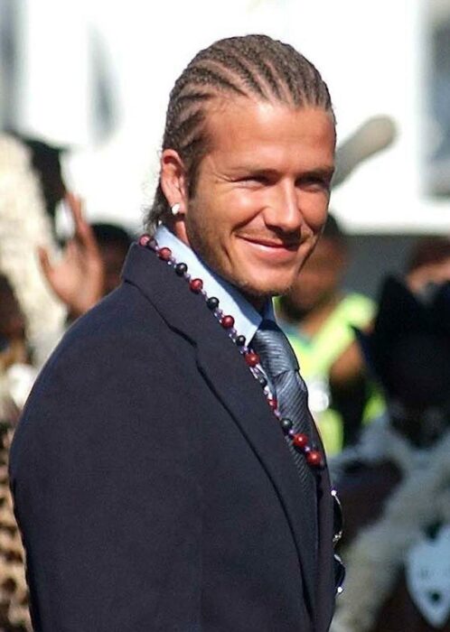 David Beckham sonríe mientras es captado con un peinado de trenzas en el cabello y lleva un traje azul marino