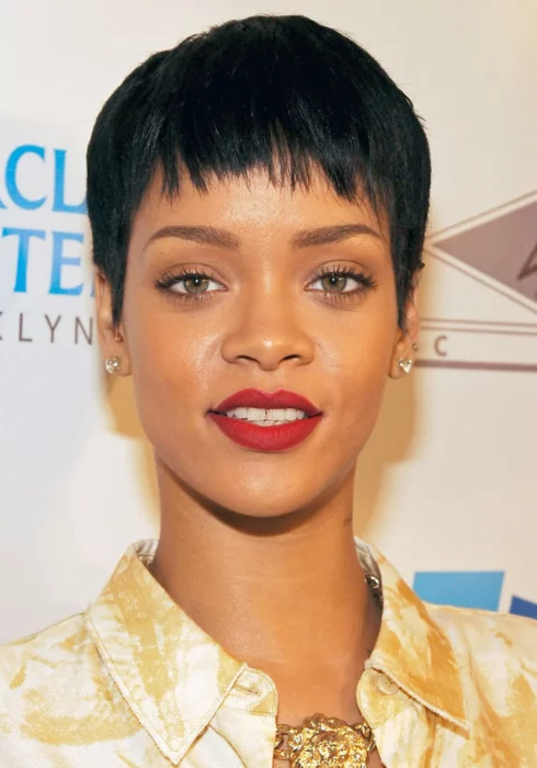 Rihanna mira de frente a la cámara con un flequillo a media frente y el cabello super corto los labios los lleva en un tono rojo