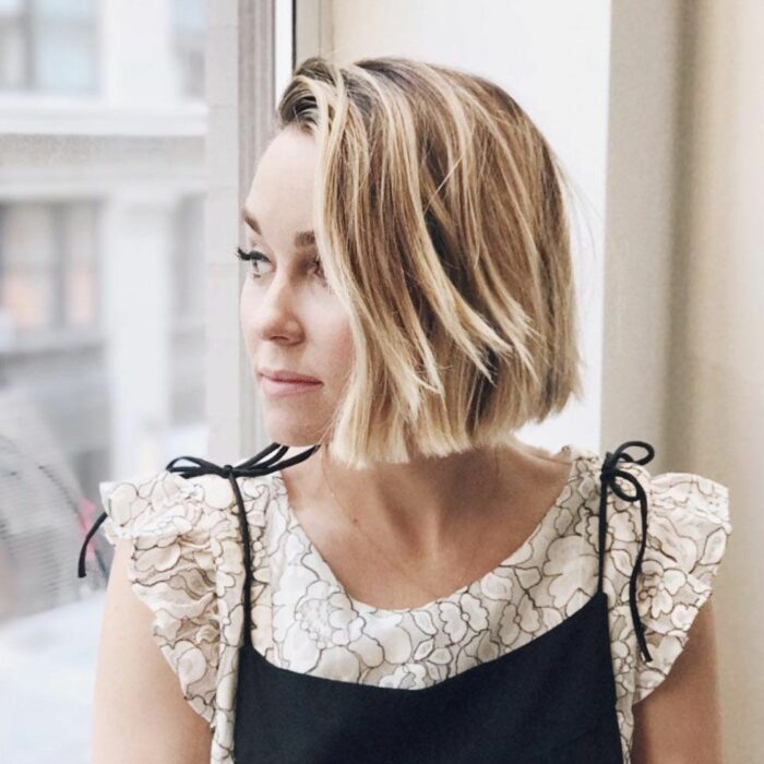 Lauren Conrad está mirando por un gran ventanal transparente lleva el cabello rubio a la altura de la barbilla