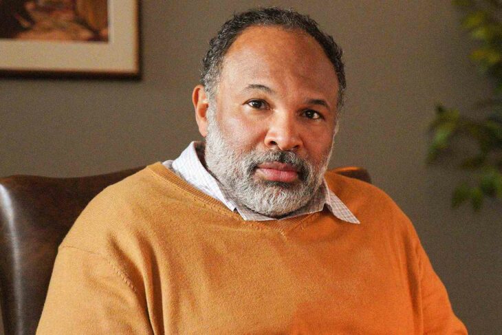 Geoffrey Owens posa con un suéter de color naranja sentado en la sala de su hogar