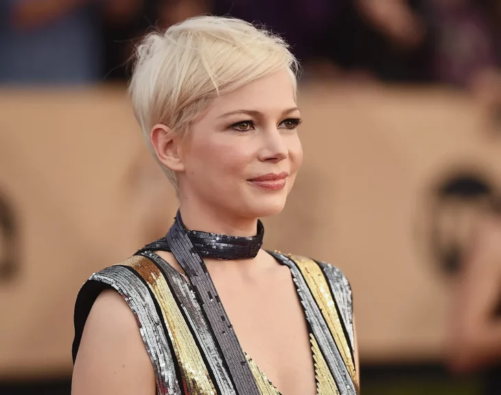 Michelle Williams en la alfombra roja de un evento de Hollywood lleva un vestido con tonos dorados y plateados tare el cabello corto y rubio