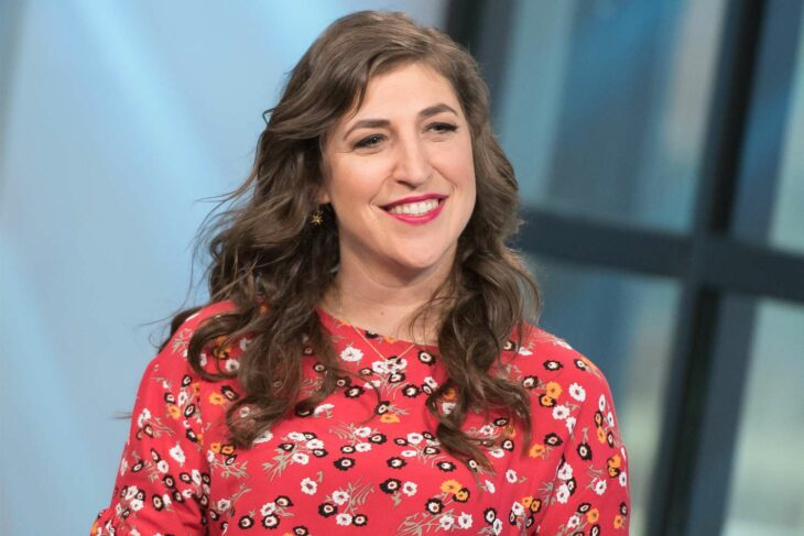 Mayim Bialik posa sonriente con un vestido floreado con base de color rojo