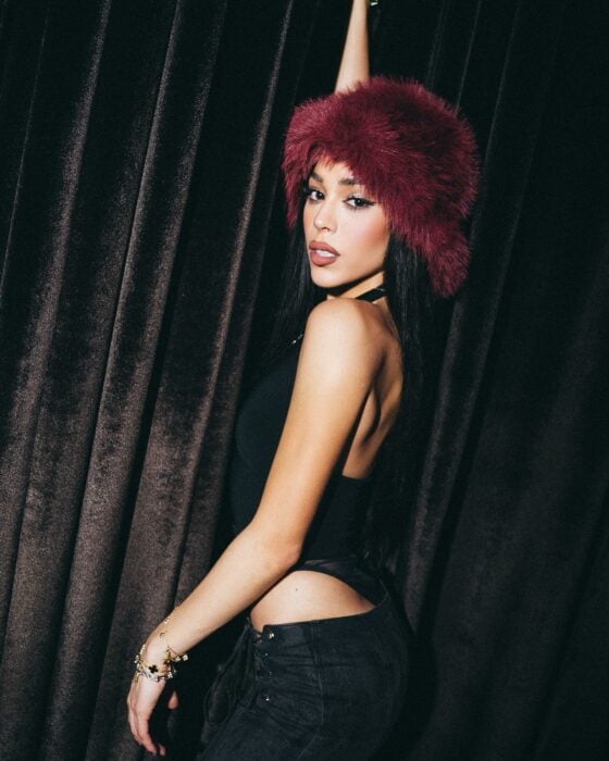 Photograph of Danna Paola posing dressed in black with a red cap on her head 