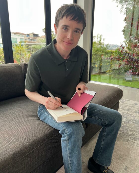 Elliot Page sentado en un sillón firmando un libro 