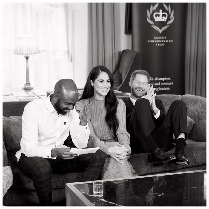 El príncipe Harry y Meghan Markle sentados en un sofá acompañados de un hombre 