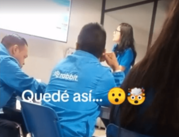 una reunión de trabajo donde se ven hombres con el uniforme de una empresa sentados en sillas azules una mujer al frente les da indicaciones