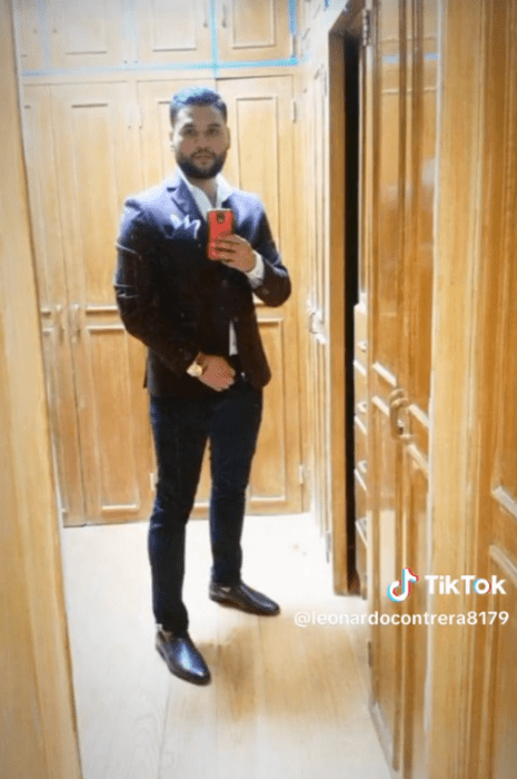 un hombre joven con traje se toma una selfi frente al espejo está rodeado del closet de madera