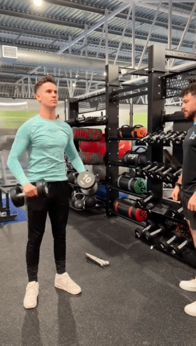 un chico está en el gym levantando pesas tipo mancuernas