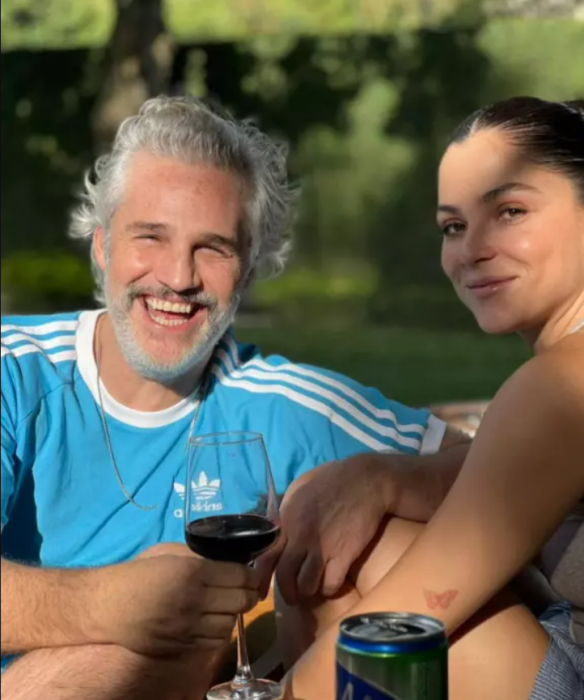 Juan Pablo Medina en una imagen junto a Paulina Dávila el actor sonríe y lleva una copa de vino tinto en la mano ella sólo hace una mueca de sonrisa